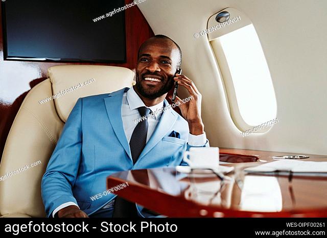 Smiling male entrepreneur talking on mobile phone while sitting private jet