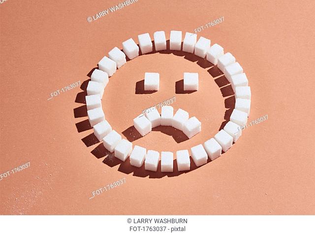 Sugar cubes forming frowning face on peach background