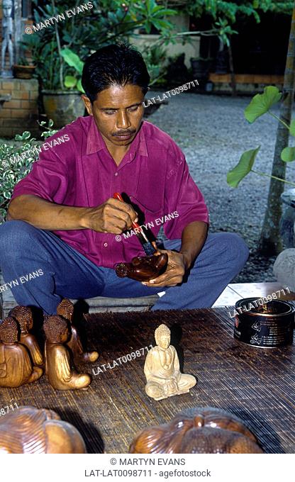 Wooden crafts shop. Man seated working. Varnishing carved wooden buddha statues