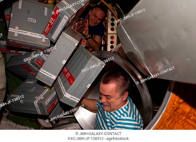 Russian cosmonauts Mikhail Tyurin and Sergey Ryazanskiy (background), both Expedition 38 flight engineers, unpack storage containers from the ISS Progress 54...