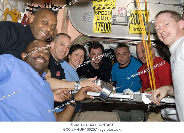 Eight of the 12 crew members currently on the International Space Station pose for a photo at the galley in the Unity node while Space Shuttle Atlantis remains...