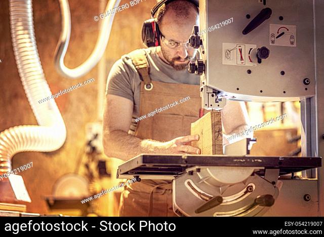 portrait of a carpenter inside his carpentry workshop using a band saw. Wear ear and eye protection