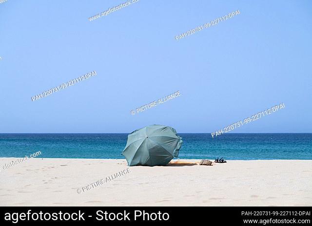 PRODUCTION - 22 July 2022, Portugal, Sagres: A green parasol is stuck in the sand on a beach in the Algarve. Photo: Viola Lopes/dpa