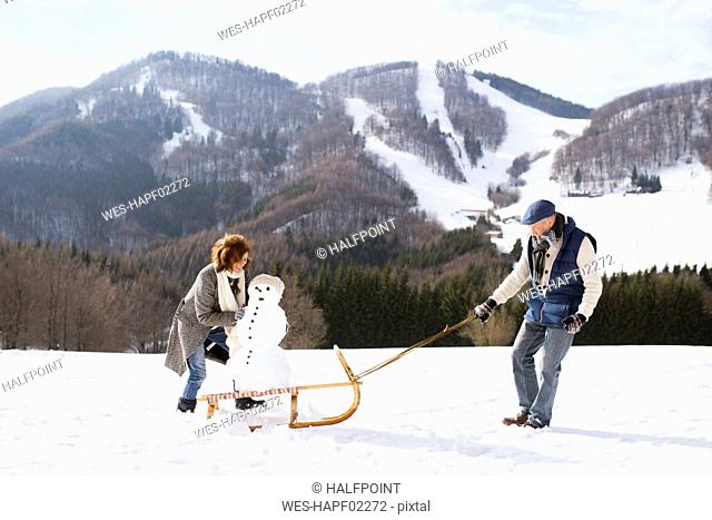 Senior couple with snowman on sledge in winter landscape
