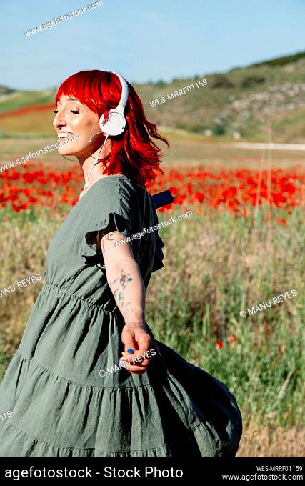 Young red-haired woman with arms outstretched enjoying sunny day on field