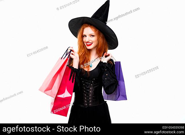 Halloween witch concept - Happy Halloween Witch smiling and holding colorful shopping bags on white background