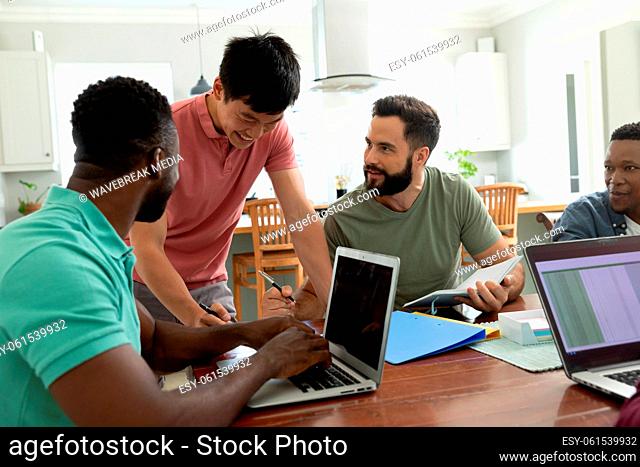 Smiling multiracial male entrepreneur talking with colleagues working at desk in office