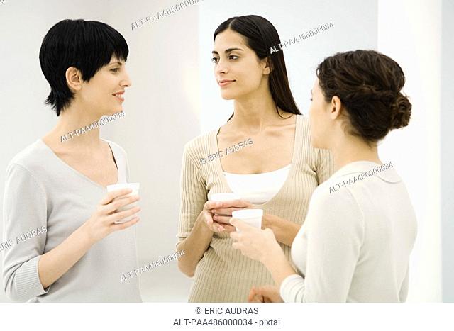 Three businesswomen chatting together, holding hot beverages