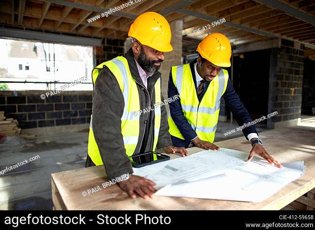 Male architect and foreman looking at blueprints at construction site