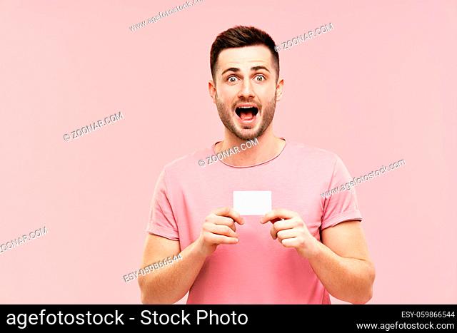 Amazed excited man with open mouth holding credit card over pink background. wow, emotions, success, winner concept