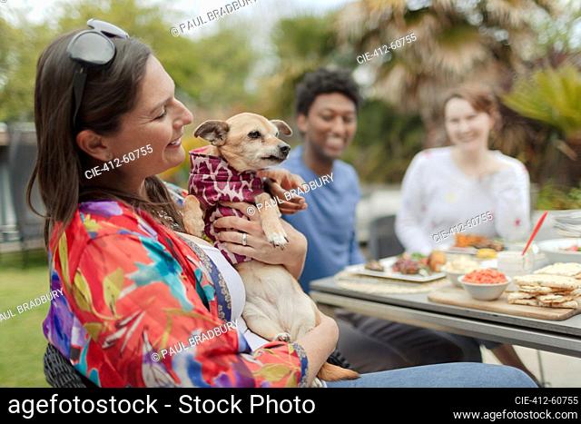 Happy woman holding cute dog at patio table