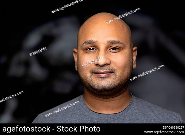Portrait of a bald man smiling against dark backdrop