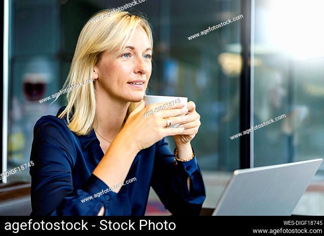 Smiling freelancer with coffee cup sitting in cafe
