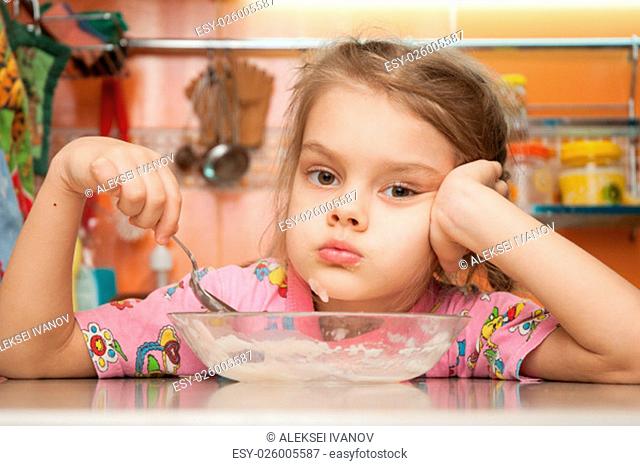Sad five year old girl in the kitchen eating cereal