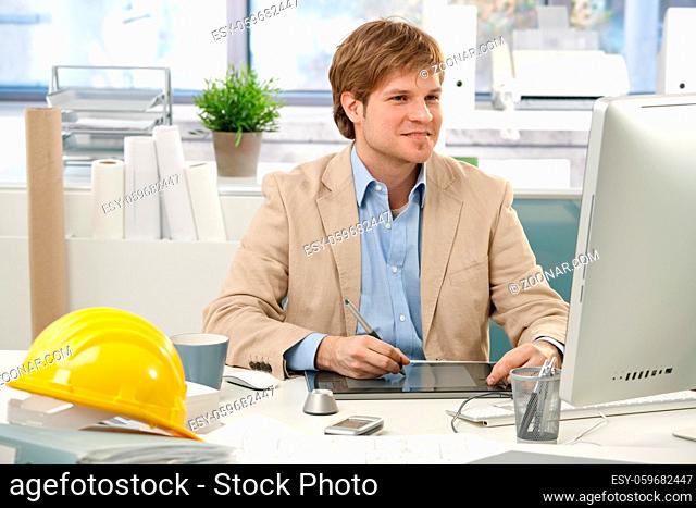 Young architect sitting at office desk, drawing pad, looking at screen