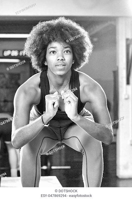 Fit young african american woman box jumping at a crossfit style gym. Female athlete is performing box jumps at gym