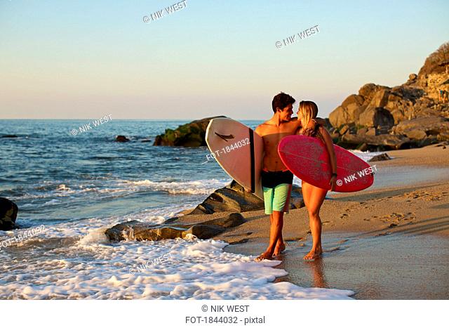 Young, affectionate couple with surfboards walking on sunny ocean beach, Sayulita, Nayarit, Mexico