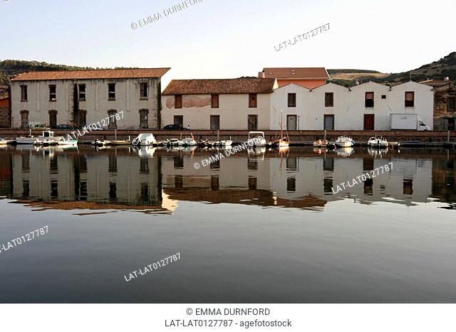 Reflections of the old tanneries with red tiled roofs on the South bank of the river Temo in Bosa with boats moored and hills beyond
