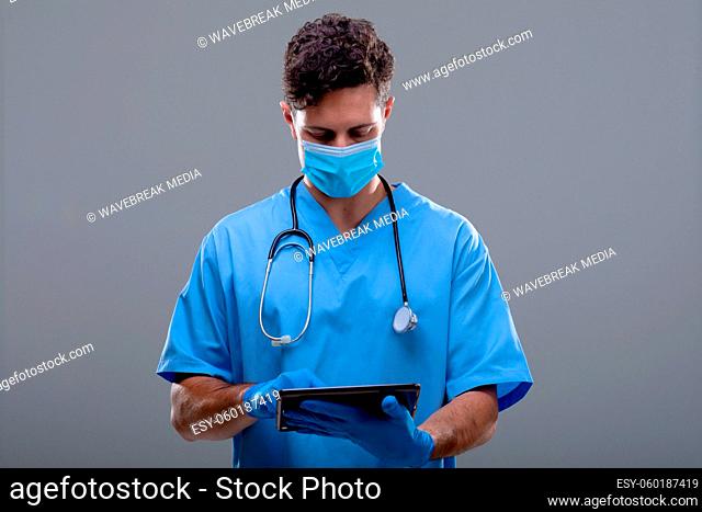 Caucasian male doctor wearing face mask using tablet