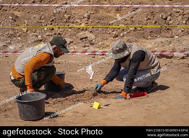 13 June 2021, Iraq, Al-Humaydat: Members of expert teams take part in the opening of a mass grave and the exhumation of the remains of victims who were killed...