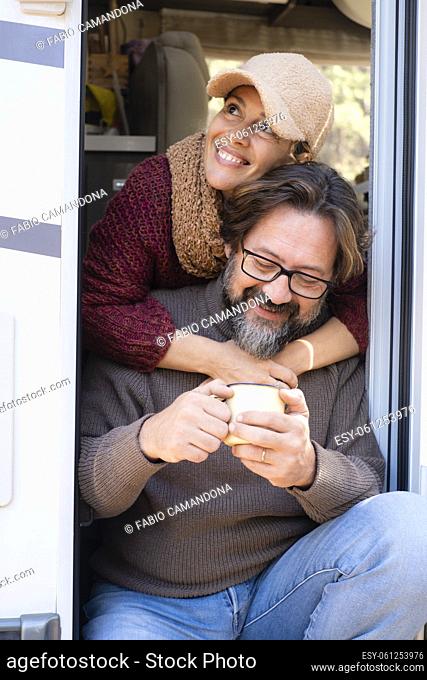Portrait of man and woman adult couple sitting on the door of a camper van and enjoying travel holiday vacation. People on the road lifestyle van life