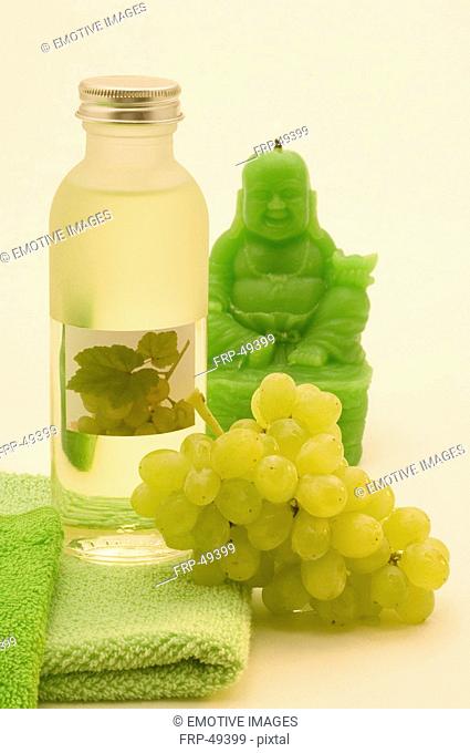 Traubenkernöl aus weißen Trauben, mit einem grünen Handtuch, weißen Weintrauben und einer grünen Buddha-Kerze