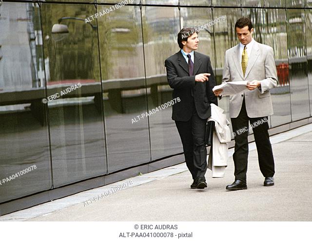 Two businessmen walking along sidewalk in front of building