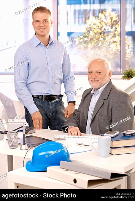Portrait of senior and junior businessmen working in office, looking at camera, smiling