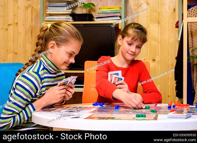 Children play a board game, one of the girls makes the next move, the other watches with a smile