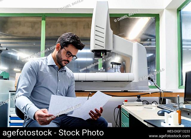 Male entrepreneur reading document while sitting in industry