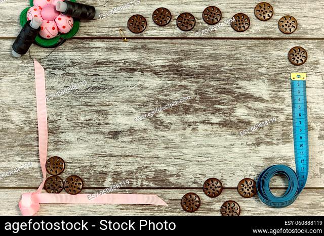 Buttons, ribbon , thread and needles for sewing . The concept of handmade sewing. On a light wooden background