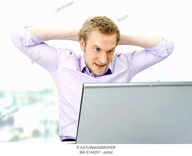 Businessman working on a laptop, arms clasped behind his head, tense