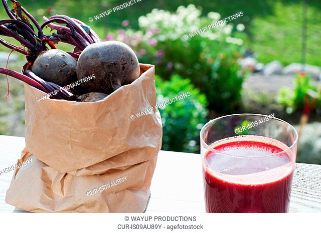 Bag of organic beetroot and glass of beetroot juice on garden table