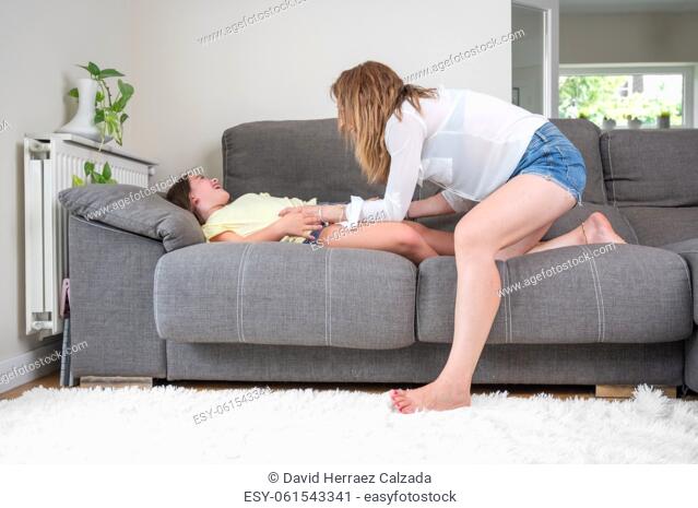 Loving mother tickling her little daughter on the sofa at home. High quality photography