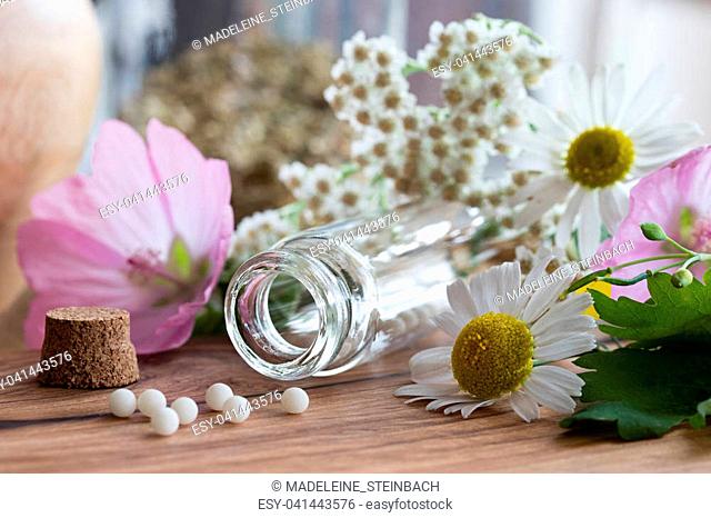 A bottle of homeopathic globules with chamomile, yarrow and other flowers in the background