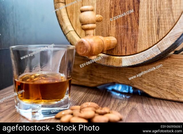 A small wooden oak barrel for home production of beer, cognac and whiskey and a glass of whiskey aged in it