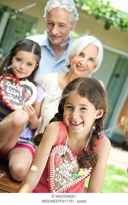 Germany, Bavaria, Grandparents with granddaughter holding gingerbread, smiling