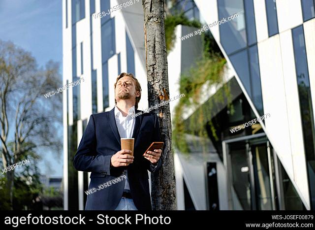 Businessman with takeaway coffee and smartphone in the city