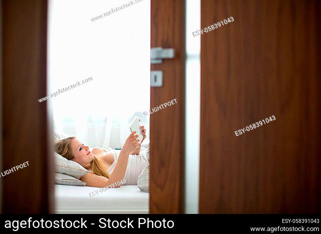 Pretty, young woman in her bed, using a tablet computer in the morning