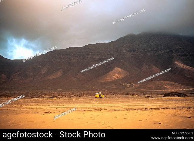 Wild and free lonely camping with old vintage scenic yellow van parked alone with beach in forehand and mountains with clouds in backgorund - travel concept...