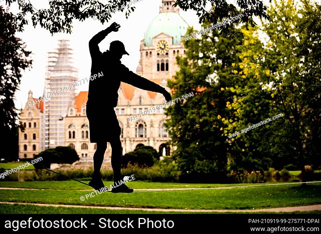 19 September 2021, Lower Saxony, Hanover: A man balances on a slackline in the Maschpark in front of the New Town Hall in cloudy weather