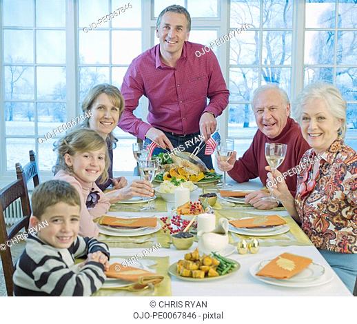 Man carving turkey for multi-generation family at table