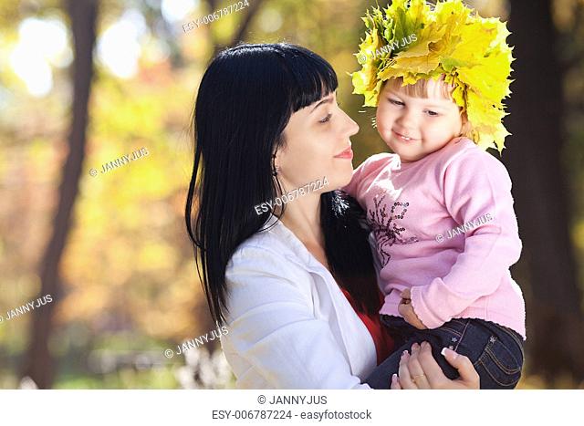 beautiful young mother holding her daughter in a wreath of maple leaves