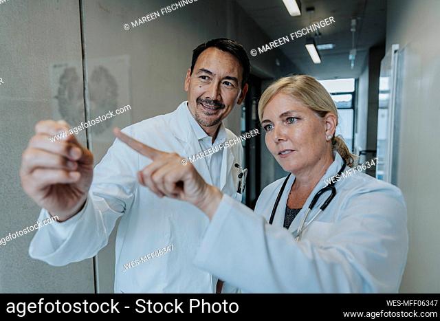 Scientist and doctor examining brain glass sample while standing at clinic corridor