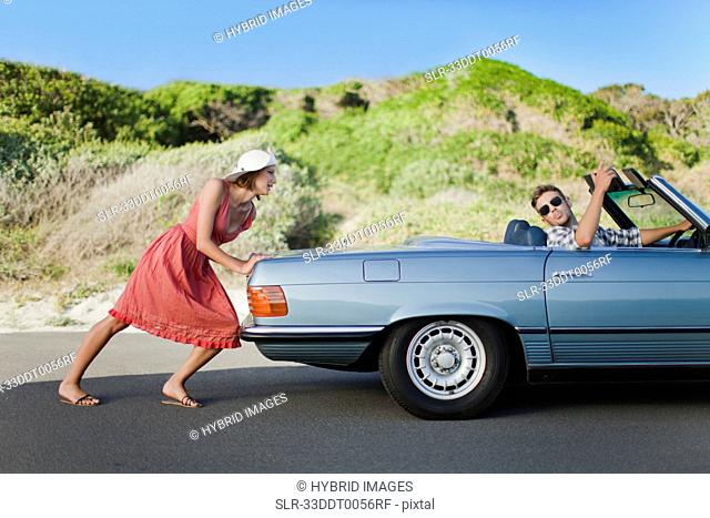 Woman pushing car as boyfriend steers