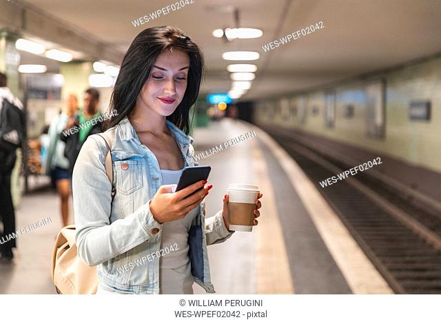 Young woman with cell phone at metro station waiting for the train, Berlin, Germany