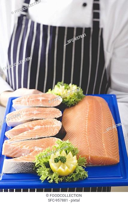 Person holding various cuts of salmon on chopping board