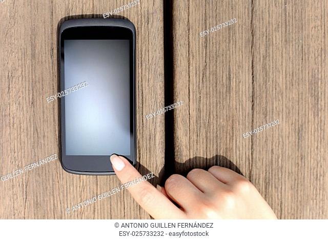 Woman finger pressing a blank smart phone touch screen with wooden background