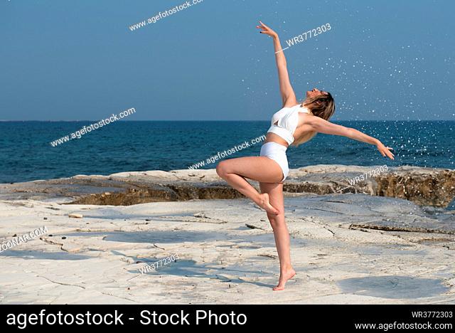 Young woman dancing outdoors on a rocky coast by the sea