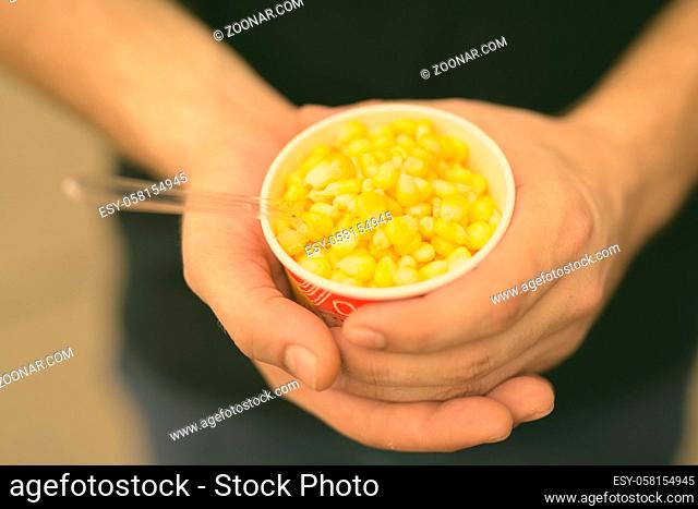 Portrait of hands of young man holding cup of deliciously steamed sweet corn